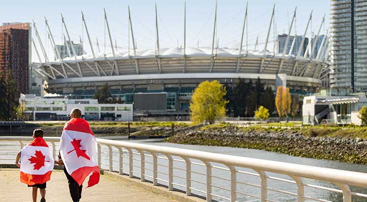 People walking along seawall with Canada flags on their backs with BC Place in the background