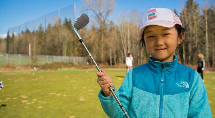 Child at a golf course holding a golf club 