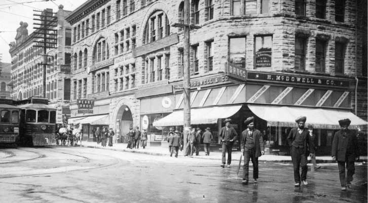Historical photo of people crossing a street with trolleys in the background