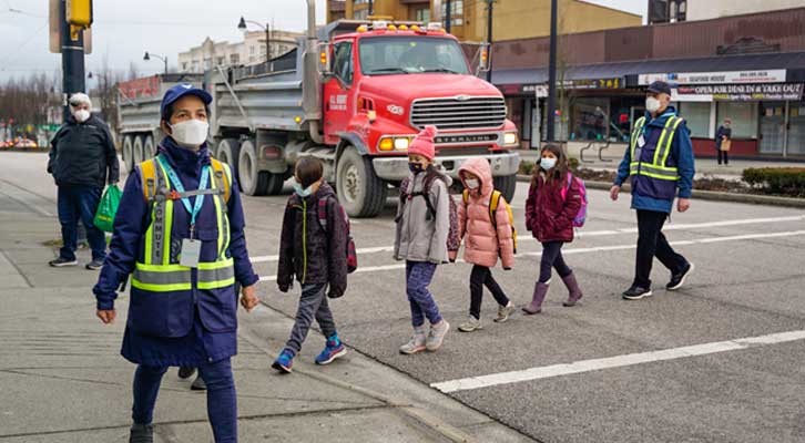 Children walking in a sidewalk across a busy street