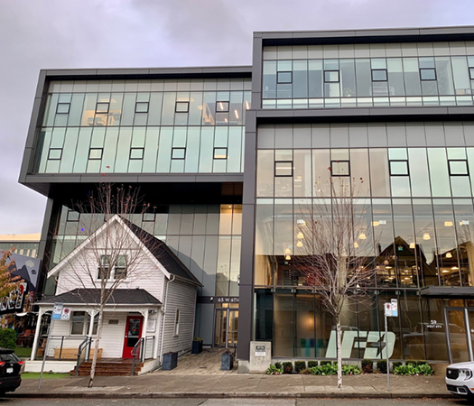 Modern office building with a preserved house integrated into its design, showing adaptive reuse.