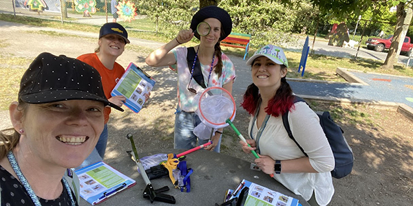 Four members of the biodiversity community science monitoring team smiling at a park table with clipboards, insect nets, and monitoring tools