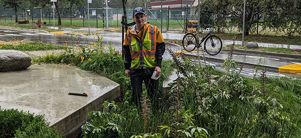 Team member in safety vest recording rainfall data in a community rain garden on a wet day