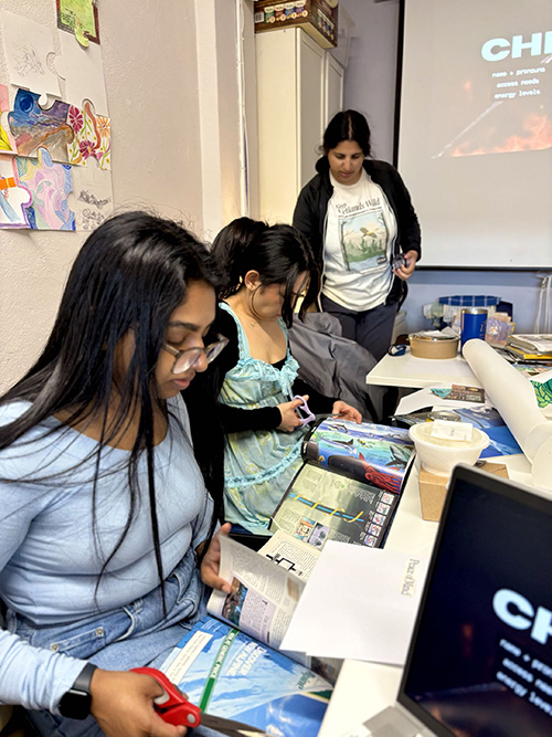 Youth participants review climate education materials at a table during an intergenerational workshop, with a facilitator standing nearby.