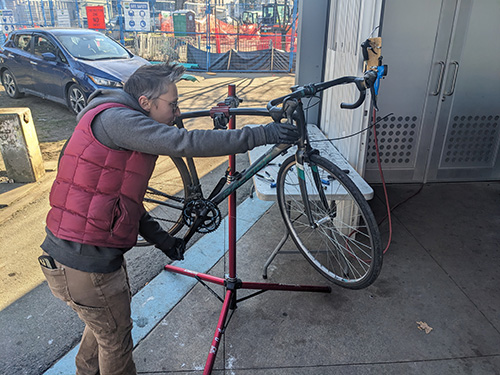 Person repairs a bicycle on a stand at an outdoor community bike clinic in the Downtown Eastside.