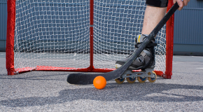Person in rollerblades holding a hockey stick with orange ball