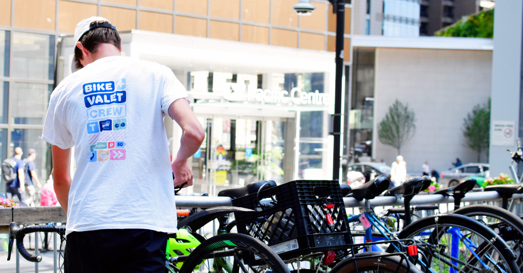 A man wearing a bike valet shirt with a row of locked bicycles