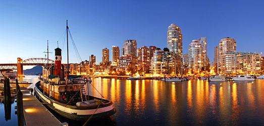 A cityscape of Vancouver at night with boats and bridges. 