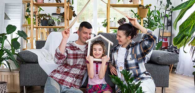 Young family, mother, father, and daughter, sitting on the floor of their living room in front of the couch. 