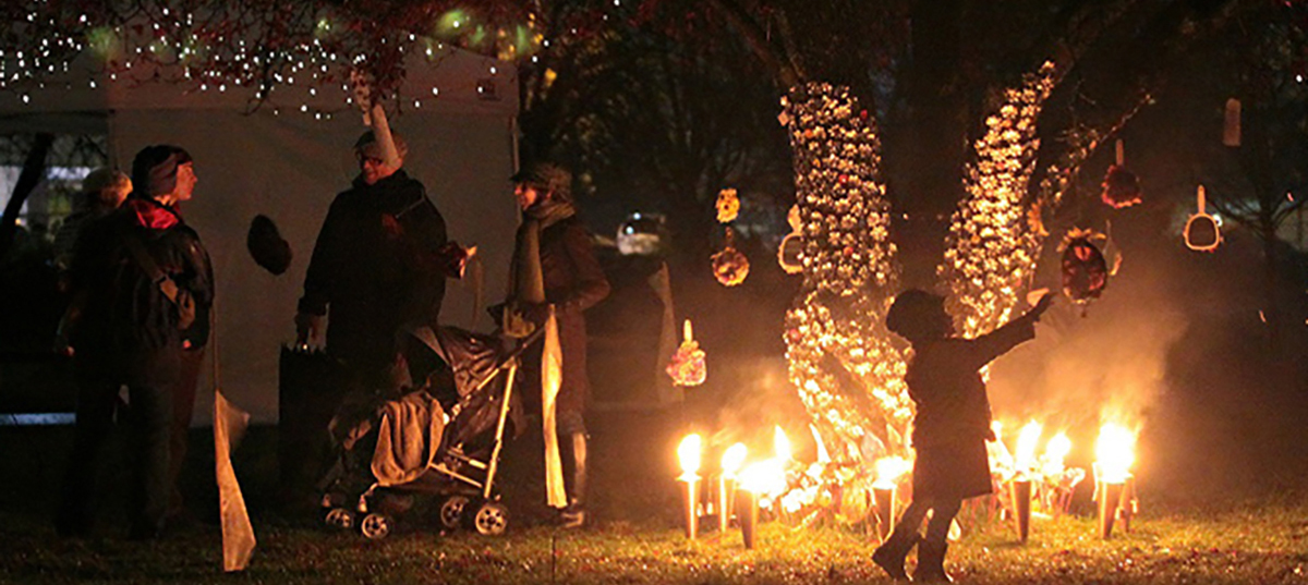 Adults and children gathering at night with candles and light displays at All Souls event at Mountainview Cemetery