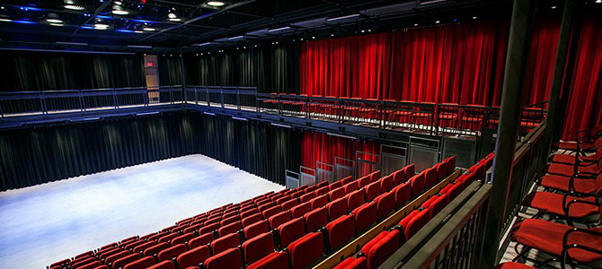Interior view of the Annex Theatre showing red seating, a flexible open performance floor, black walls, and an upper balcony with additional seating.