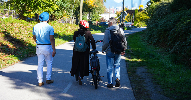 Three people walking along the Arbutus Greenway, one person has a bike.