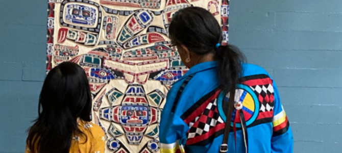 Two people looking at an Indigenous art piece