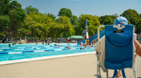 A person sits on a beach chair at Vancouver's Second Beach Pool with swimmers in the background
