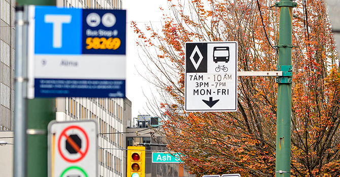 A rush hour zone sign behind a bus stop sign