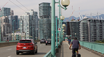 A cyclist on the Cambie Bridge bike lane alongside cars on a bridge with city buildings in the background.