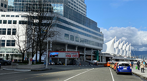 Canada Place and street with pedestrians, cars, and mountains in the background.