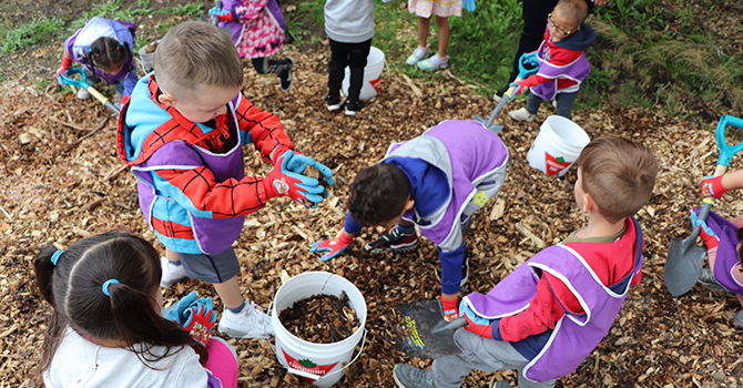 Children gathering mulch and putting it in a bucket