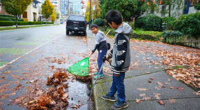 Two children raking leaves on the street standing on the sidewalk