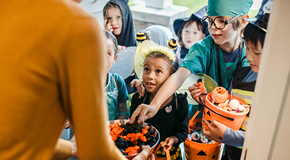 Children in Halloween costumes collect candy in pumpkin-shaped buckets while trick-or-treating