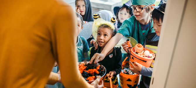 Children in Halloween costumes collect candy in pumpkin-shaped buckets while trick-or-treating