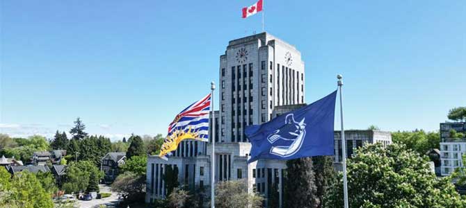 City hall building with BC and Canucks flags flying in front of the building