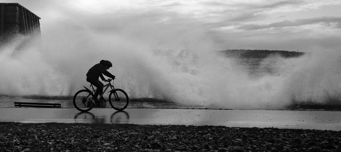 A person biking along the seawall with big waves in the background