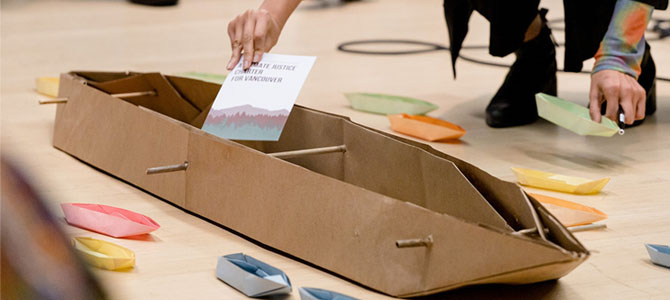 A person putting a document in a cardboard boat with small paper boats around it.