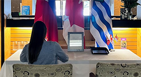 A person seated at a condolence book signing table with Canadian, Philippine, and British Columbian flags behind them.