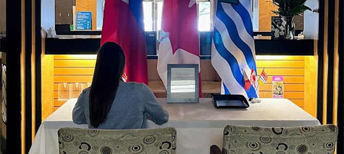 A person seated at a condolence book signing table with Canadian, Philippine, and British Columbian flags behind them. A person seated at a condolence book signing table with Canadian, Philippine, and British Columbian flags behind them.