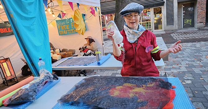 A woman uses a bottle of dish soap to create a art at a street craft fair event.