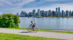 Person cycling along a waterfront bike path with the Vancouver skyline in the background on a sunny day