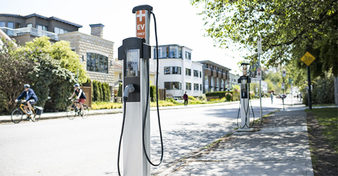 An EV station on a bright and busy street with cyclists passing by