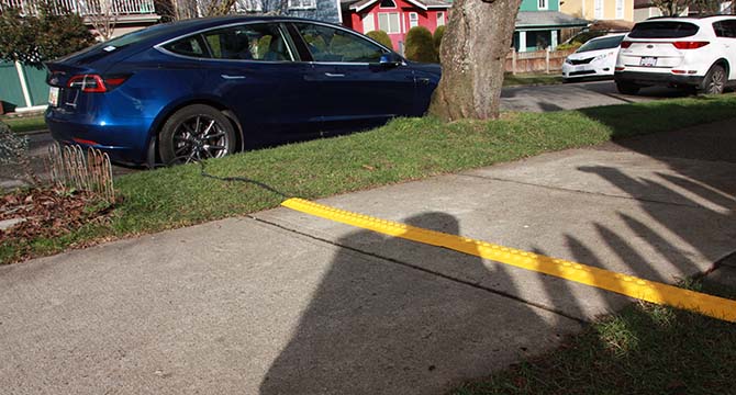 Electric vehicle charging cord cover on a sidewalk