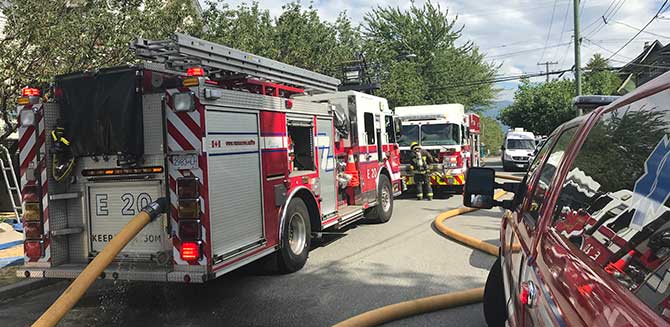 Fire truck with a hose on a street in front of a house