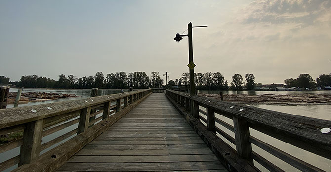 Wooden pier extending over water with a lamppost and trees in the distance
