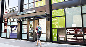 Man walking on a sidewalk past a storefront with a sign that reads 