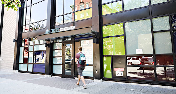 Man walking on a sidewalk past a storefront with a sign that reads 