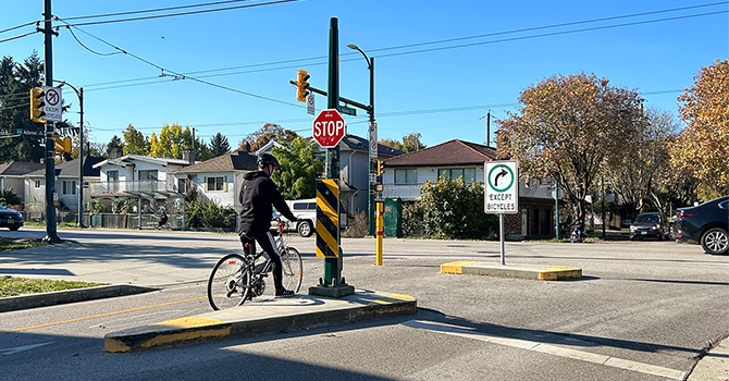 A cyclist patiently waits by a stop sign at an urban intersection, ready to proceed when it's safe to do so.