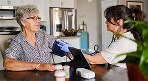 A healthcare worker checks the blood pressure of an older woman at home.