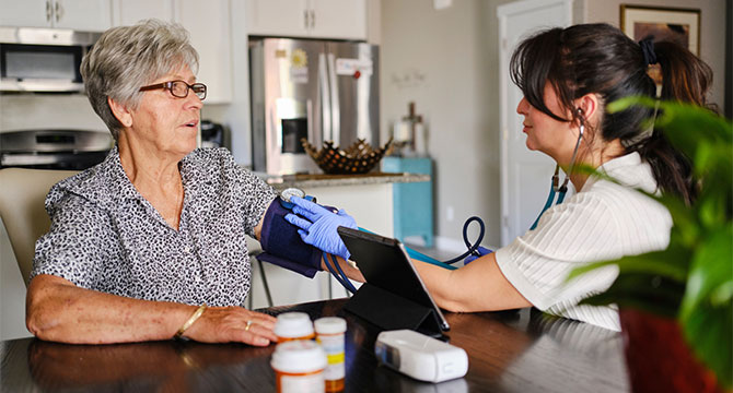 A healthcare worker checks the blood pressure of an older woman at home.