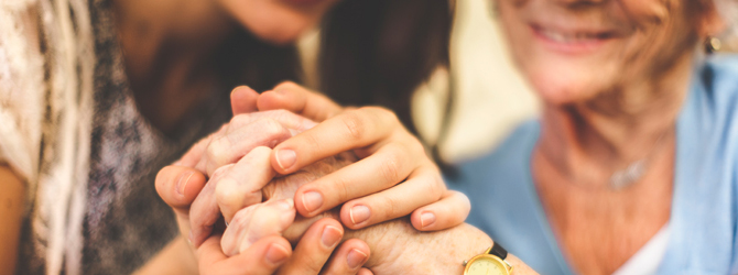 People holding an older adult’s hands in a supportive gesture