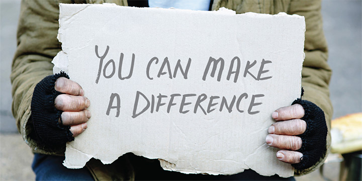 Person who is homeless holding a cardboard sign that reads 'you can make a difference'