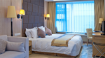 Furnished hotel room with a large bed, desk, chair, and a seating area by the window.
