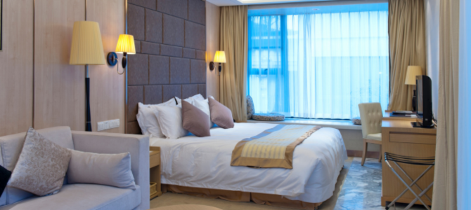Furnished hotel room with a large bed, desk, chair, and a seating area by the window. Furnished hotel room with a large bed, desk, chair, and a seating area by the window.