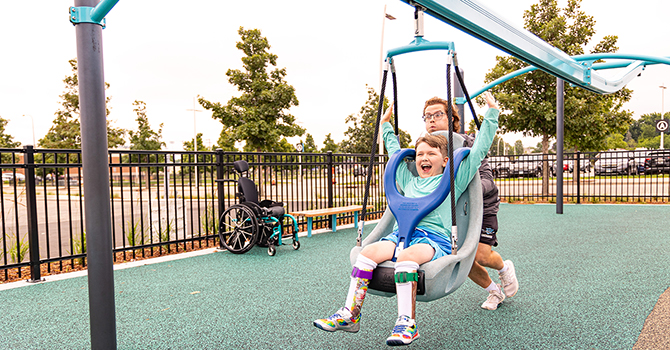 Child on a playground zipline, smiling while an adult runs alongside.