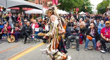 An Indigenous person dances at a festival with many onlookers 
