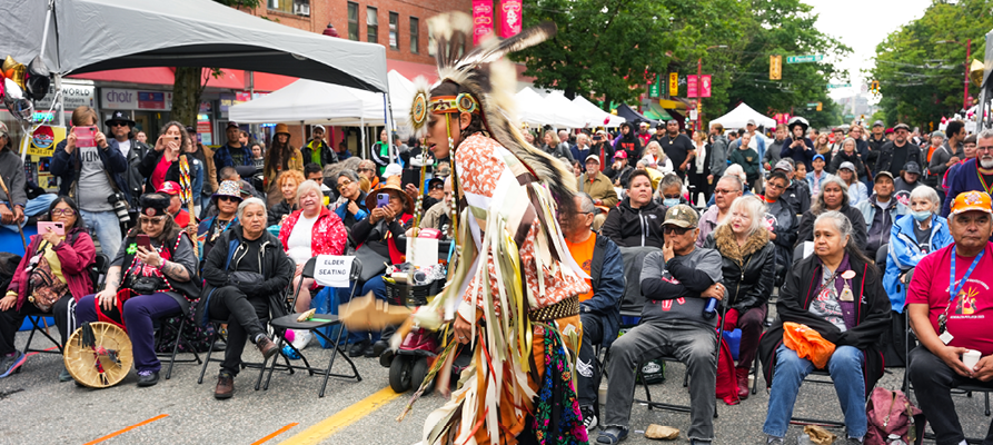 An Indigenous person dances at a festival with many onlookers An Indigenous person dances at a festival with many onlookers