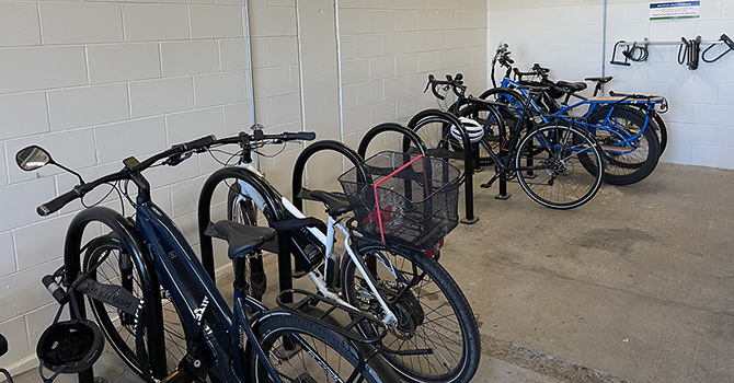 Indoor bike parking room with upright racks, a variety of bicycles, and wall-mounted hooks in the background. Indoor bike parking room with upright racks, a variety of bicycles, and wall-mounted hooks in the background.