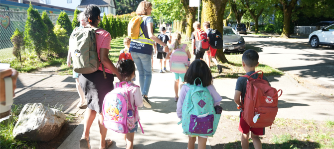 Kids and adults walking on a sidewalk through a sunny neighbourhood Kids and adults walking on a sidewalk through a sunny neighbourhood